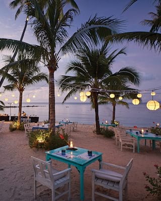 Informal beach restaurant at sunset, surrounded by palms and hanging lanterns